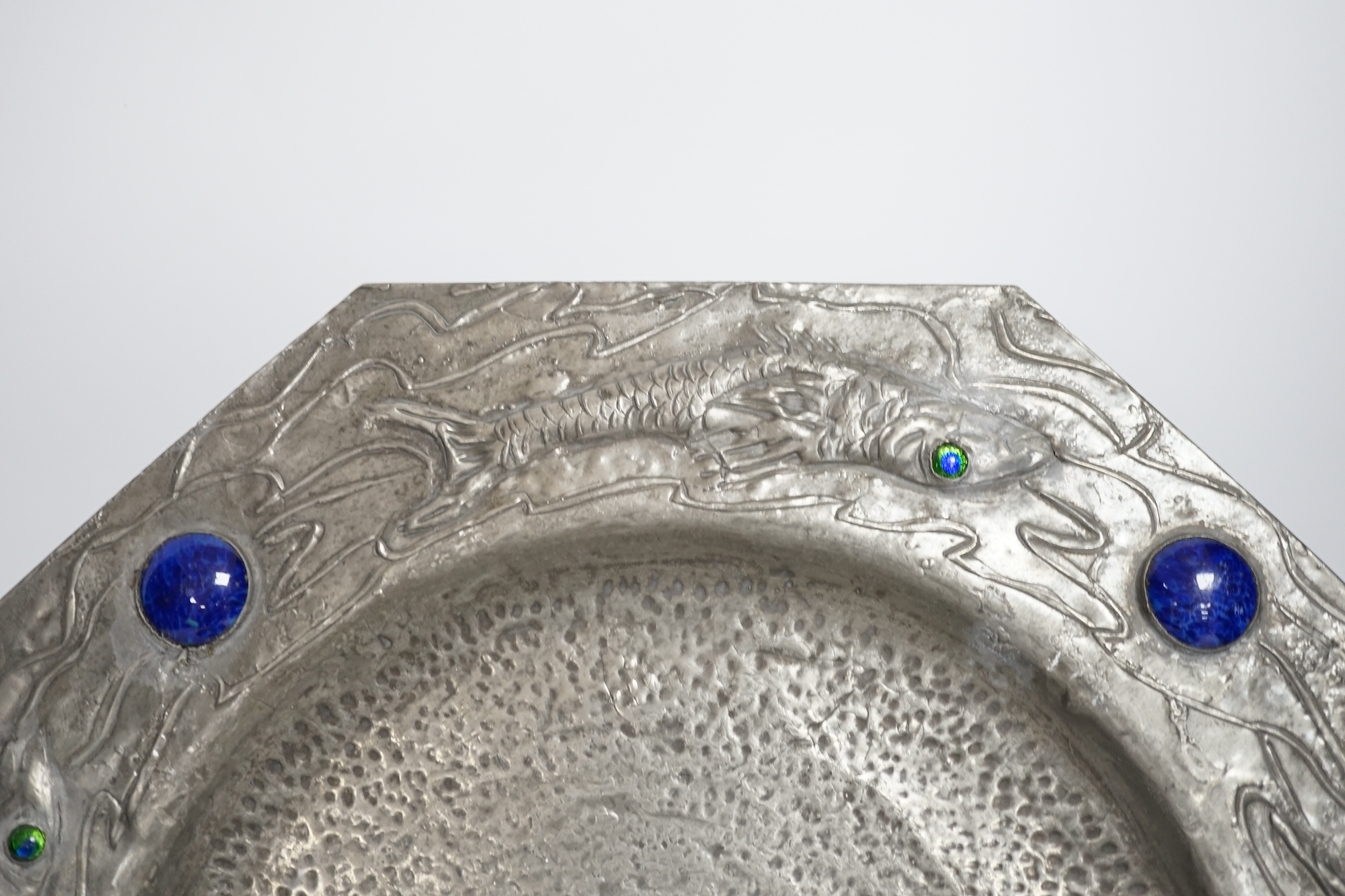 An Arts and Crafts style pewter fish plate with ceramic insets and glass eyes together with a pottery armorial charger, pewter charger 35cm wide